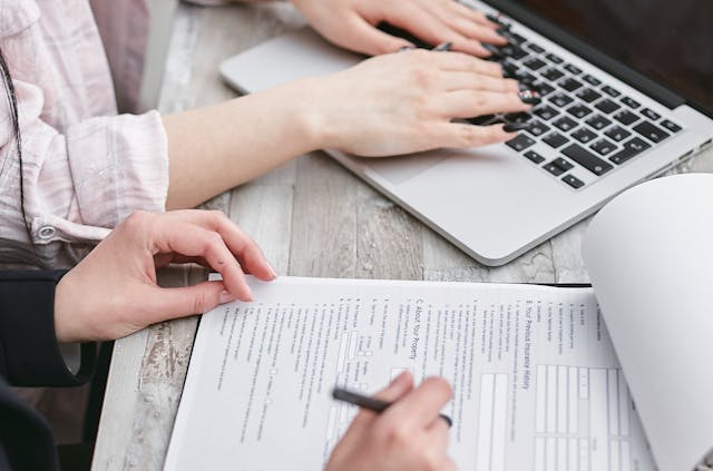 Person writing on a document while a person types on a laptop